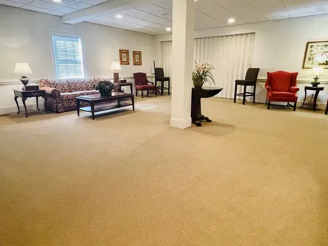 Spacious beige-carpeted living room with sofas, chairs, white columns, and soft lighting
