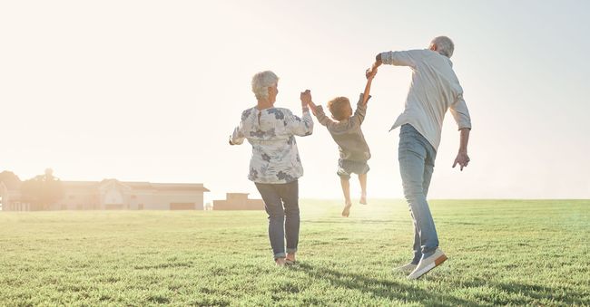 Three people running hand in hand across a sunlit grassy field