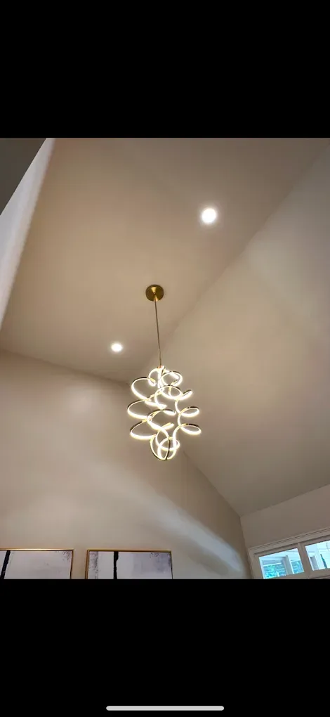 A modern chandelier hangs from a beige sloped ceiling, lit by two recessed lights.