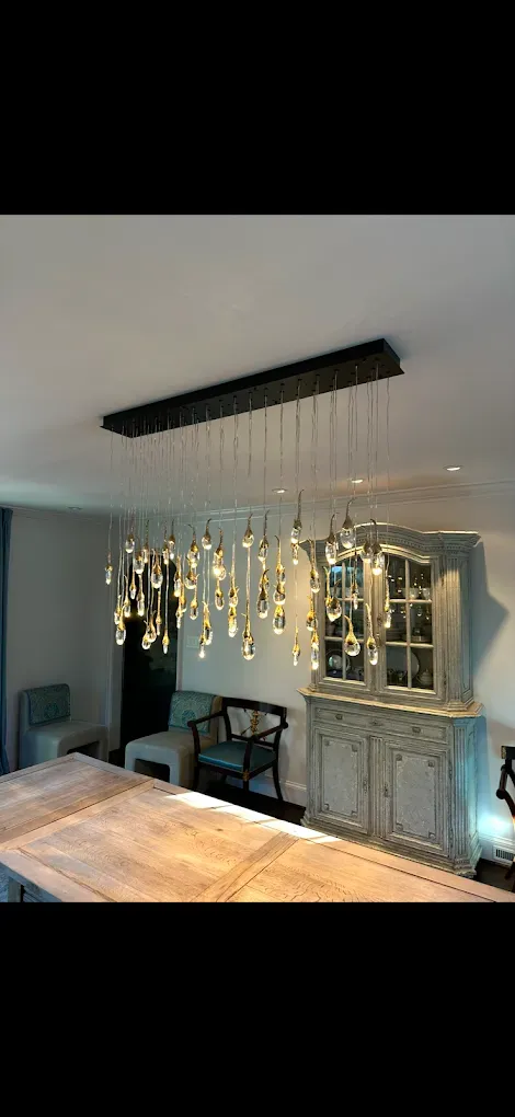A dining room with a long wooden table, a crystal chandelier, and a white cabinet.