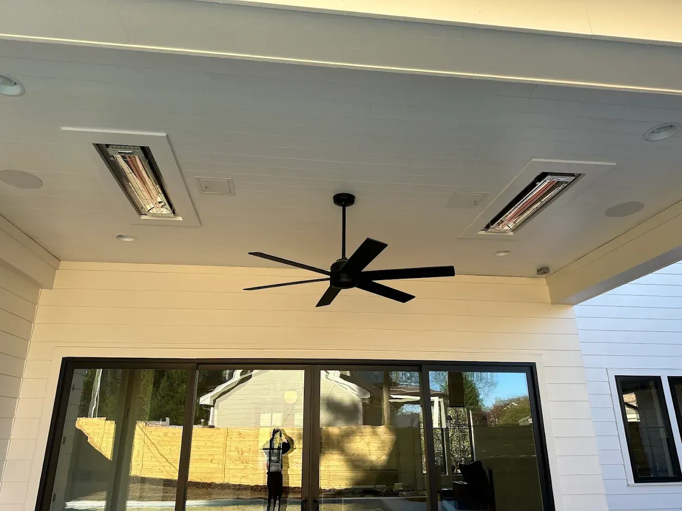 Outdoor patio with black ceiling fan, two heaters, and glass sliding doors.