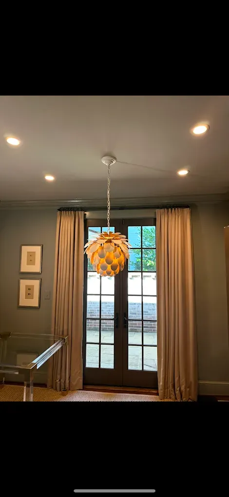 A room with a pendant light, door, windows, and curtains. Light-colored curtains frame the doorway.