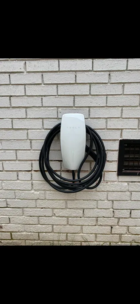 White electric vehicle charging station mounted on a white brick wall, with a black cable coiled below it.
