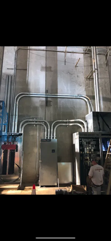 Electrical wiring in conduits running along a concrete wall, with a man standing nearby.