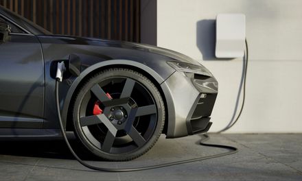 Gray electric car charging from a white wall-mounted charger outdoors.