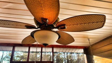 Ceiling fan with wicker blades and a light fixture, mounted on a wood-paneled ceiling.