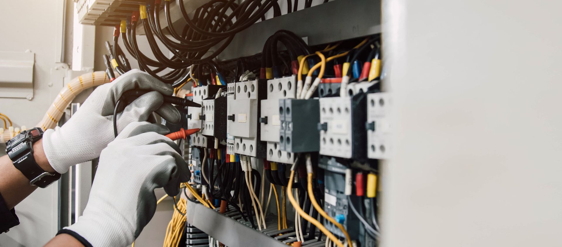 Person in gloves using a tool to work on electrical wiring in a panel.