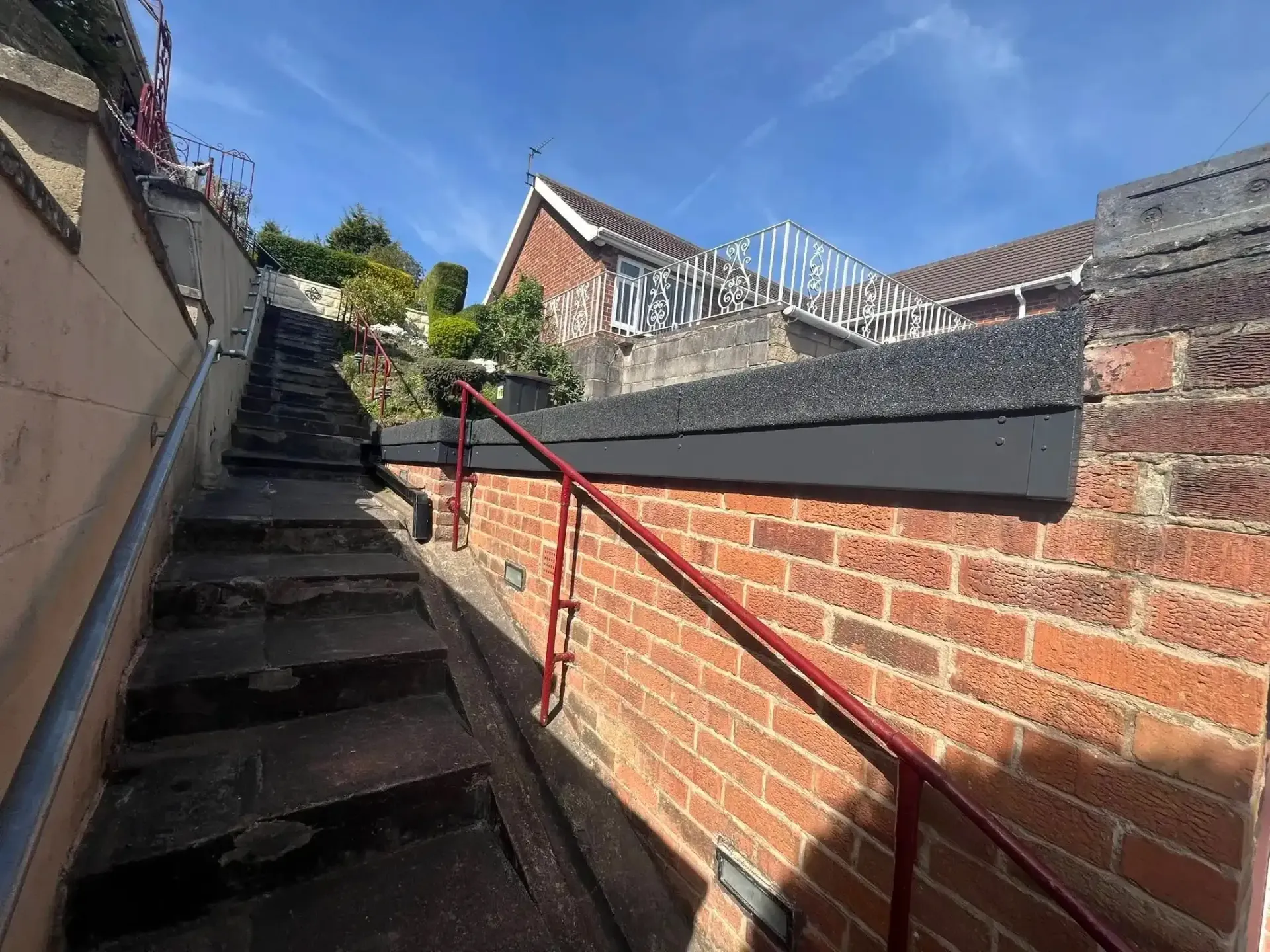 Steep outdoor brick stairway with red handrail between walls under a blue sky