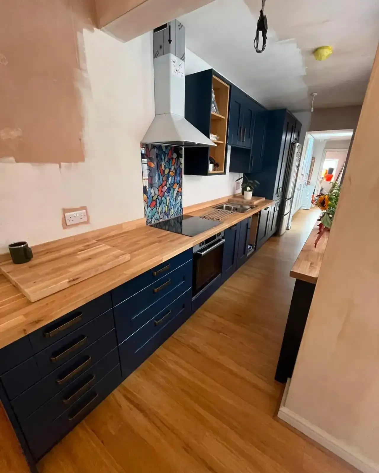 Narrow kitchen corridor with blue cabinets, wooden countertops, tiled backsplash, and open shelves under renovation