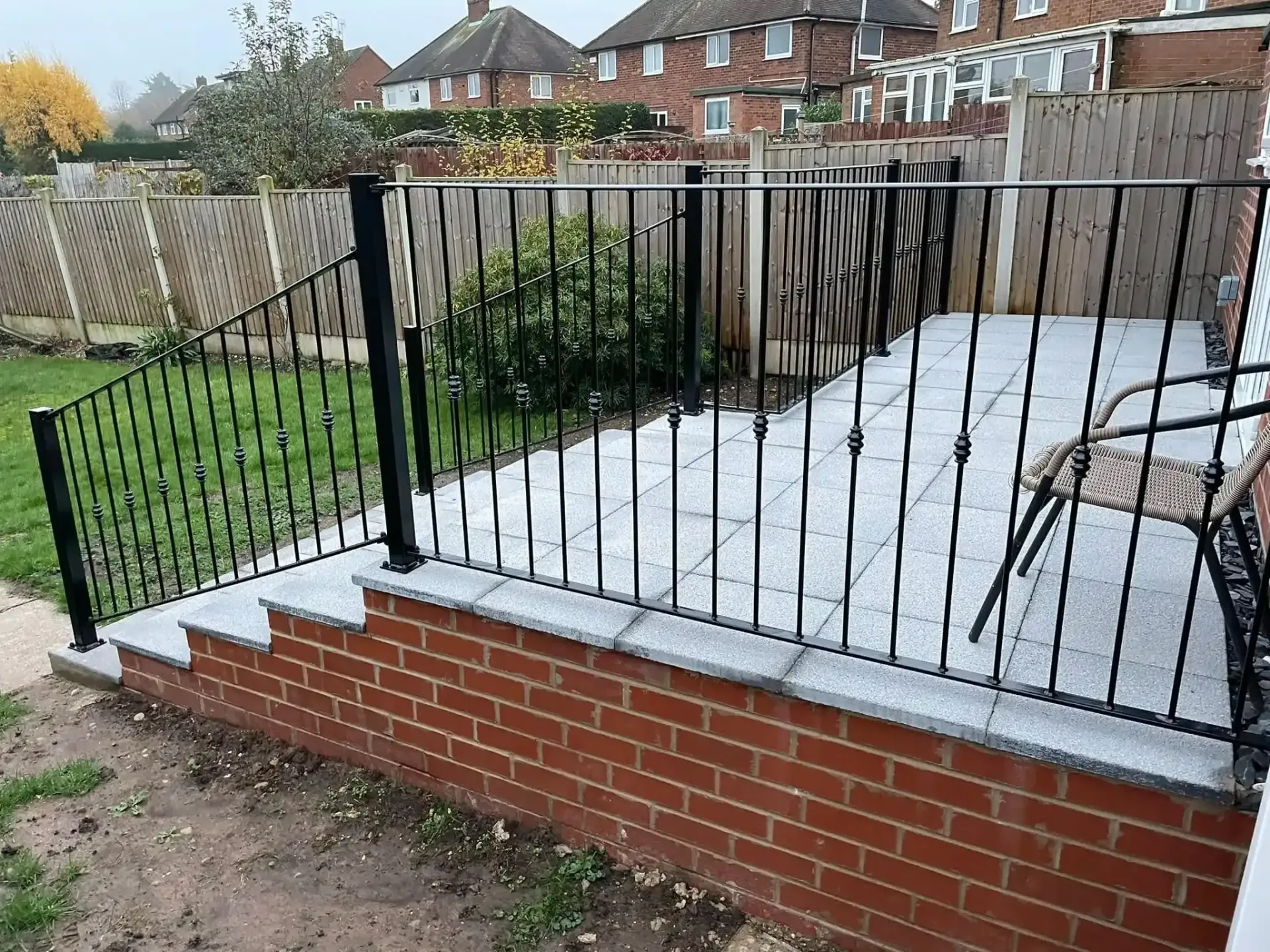 Brick front wall with black metal railings along a sloped driveway and small garden.