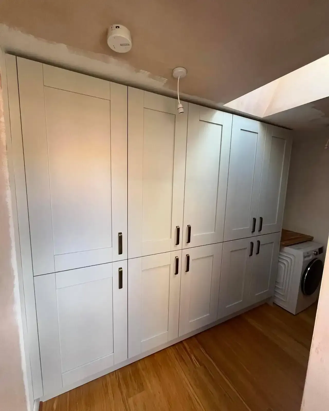 White built-in wardrobe cabinets in a room with wood floor and a washing machine at the side.