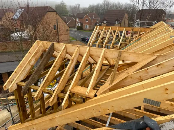 Wooden roof trusses under construction on a house, with rooftops and trees in the background
