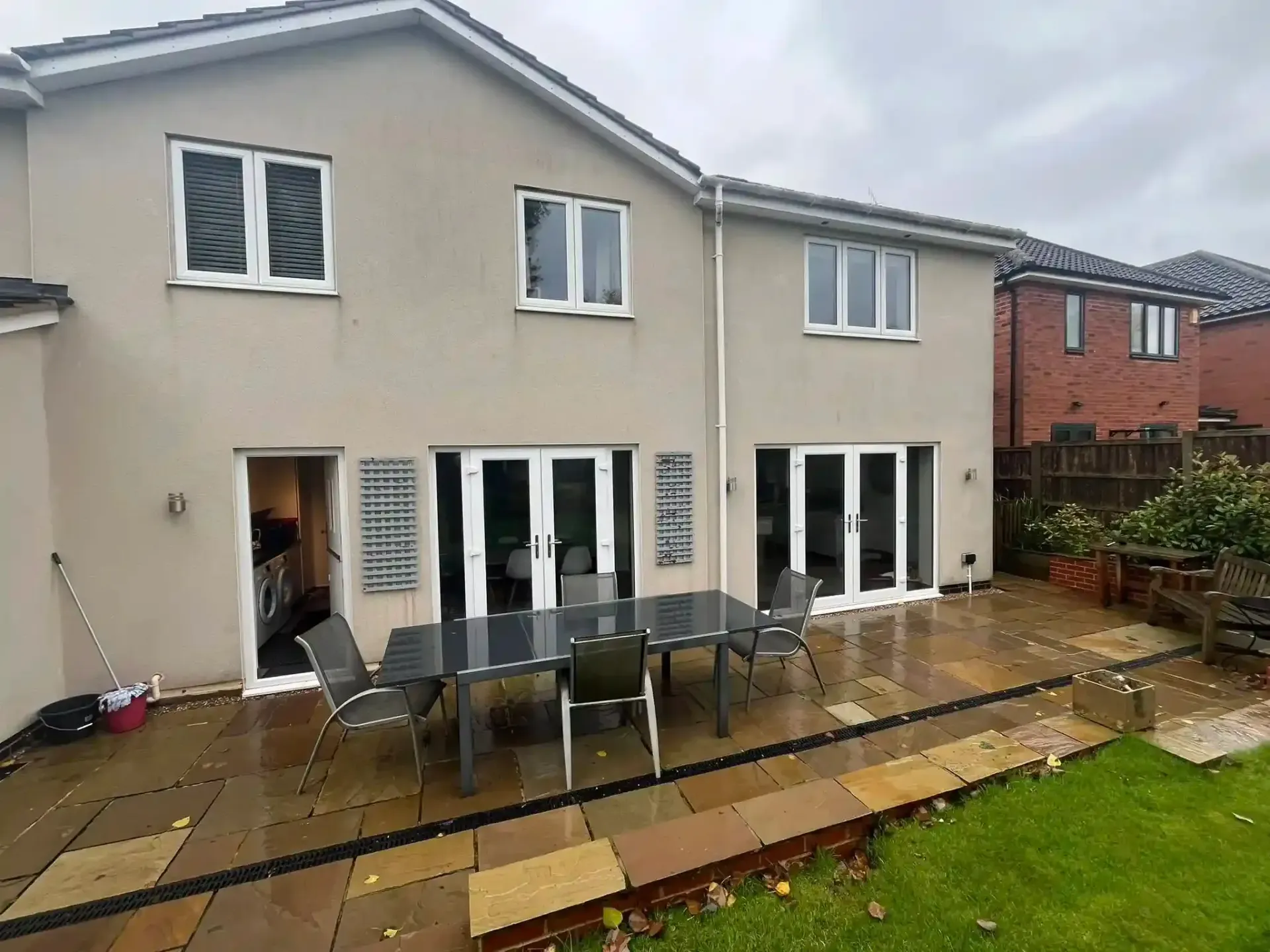 Patio with outdoor dining set beside a beige two-story house and sliding doors after rain