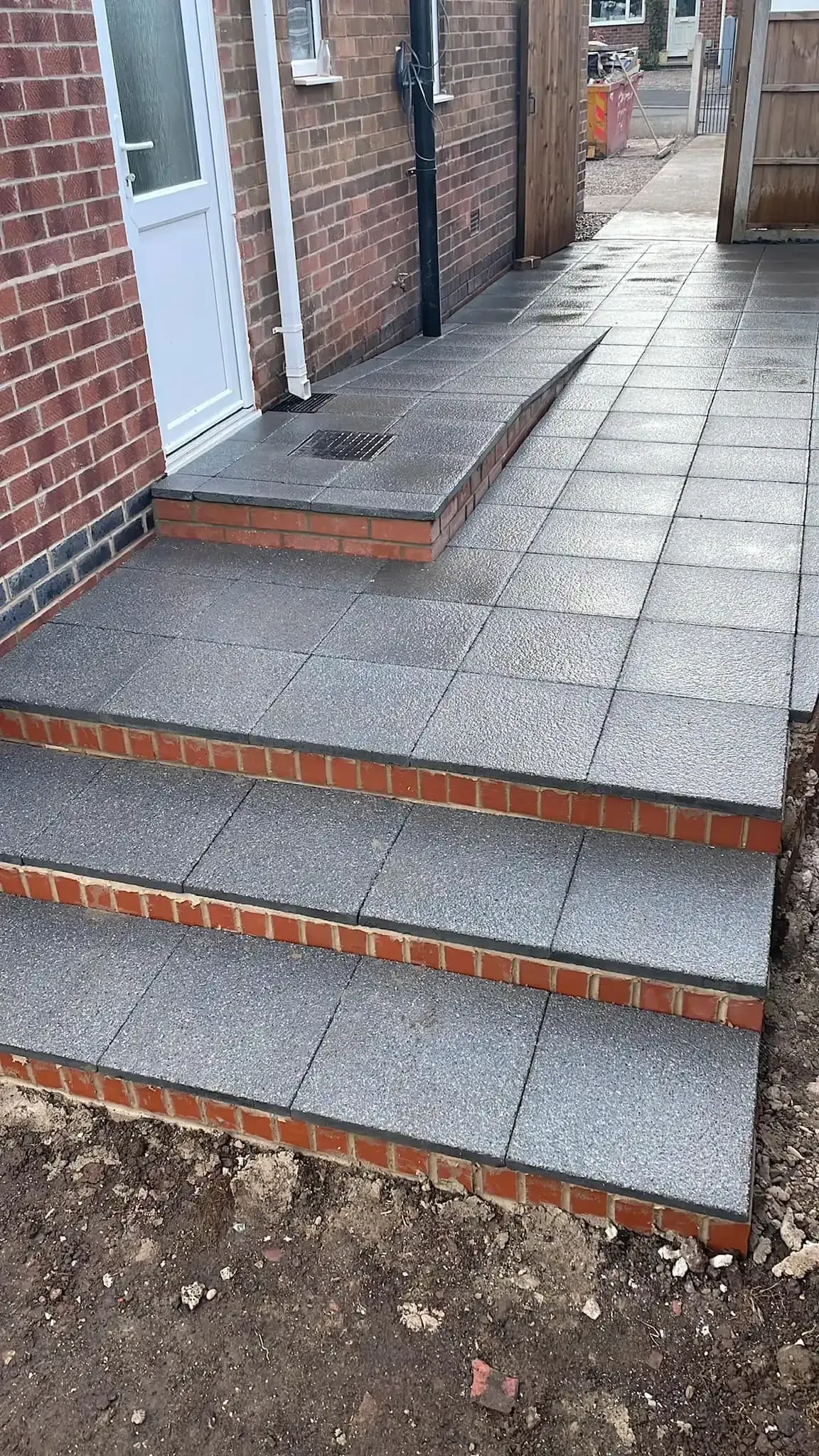 Brick building entrance with three concrete steps and a narrow walkway beside it.
