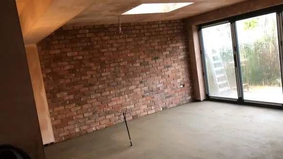 Empty room with brick accent wall, concrete floor, and sliding glass doors to a patio.