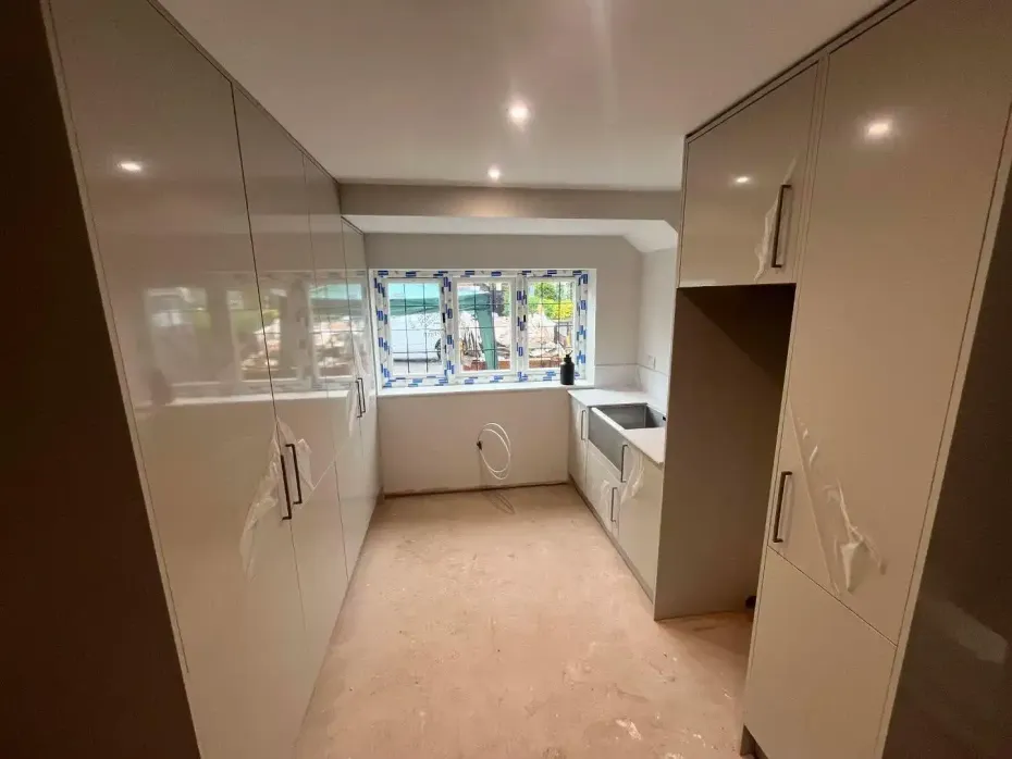 Narrow modern kitchen with glossy beige cabinets, white countertop, and window above the sink