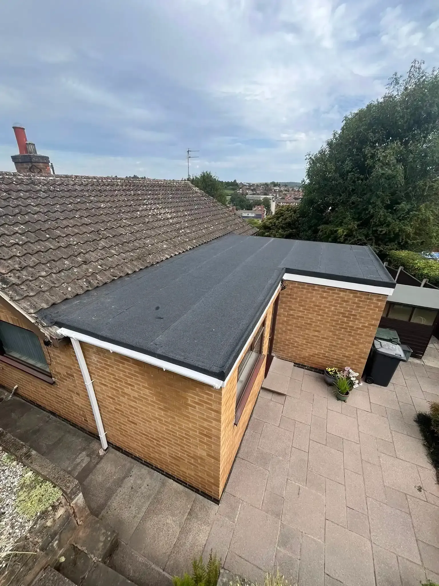 Aerial view of a small brick garage with a dark roof and gravel driveway beside a house.