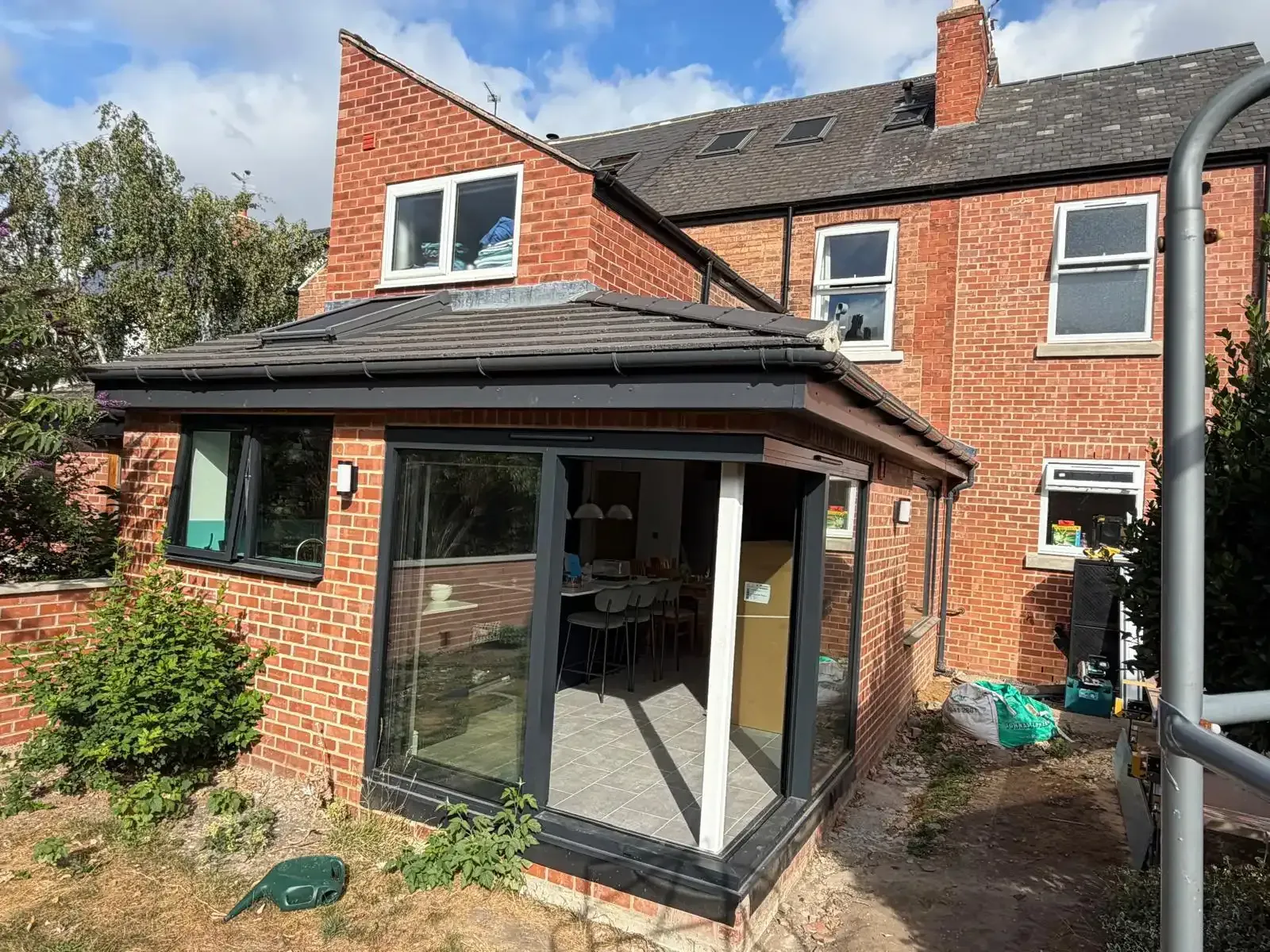 Brick house extension with black-framed glass doors and windows under a gray roof