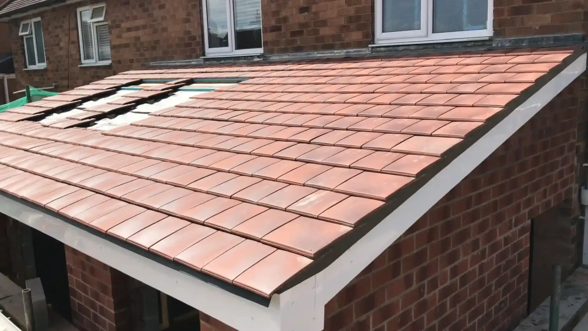 Brick house roof with terracotta tiles and several damaged sections near the ridge