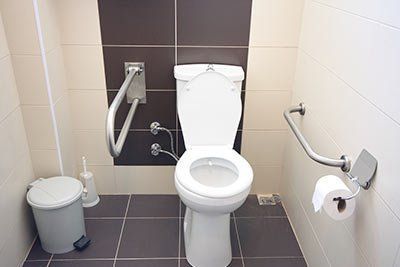 Accessible restroom stall featuring a white toilet with grab bars on both sides and a small trash bin.