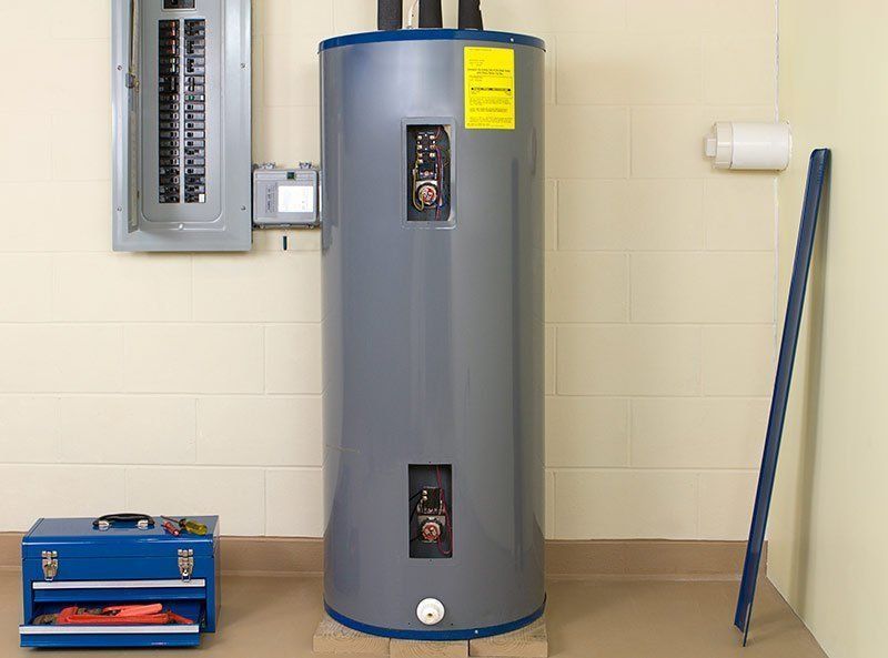 A gray electric water heater stands in a room beside an electrical panel, a blue toolbox, and a metal support bar.