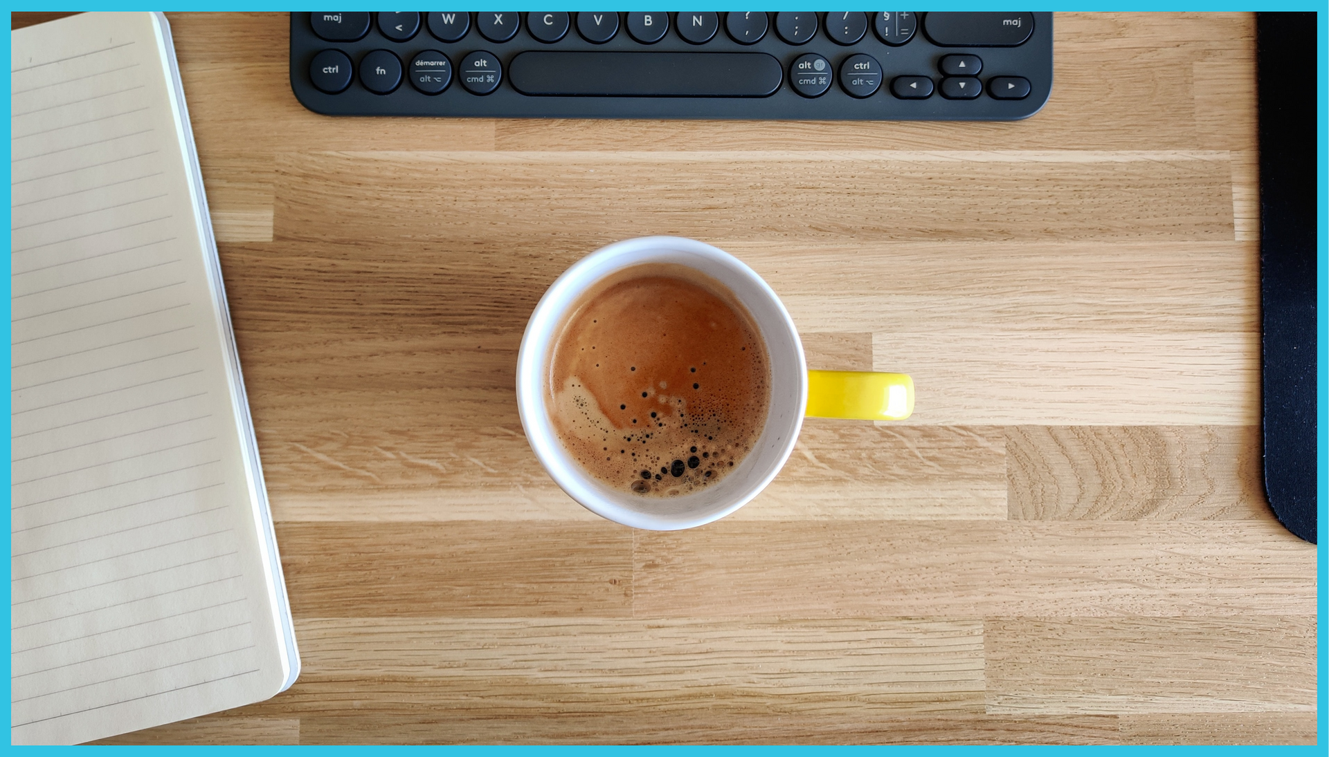 A cup of coffee is sitting on a wooden table next to a keyboard.