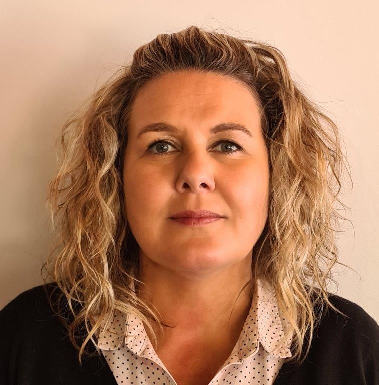 A woman with curly hair is wearing a polka dot shirt and a black sweater.
