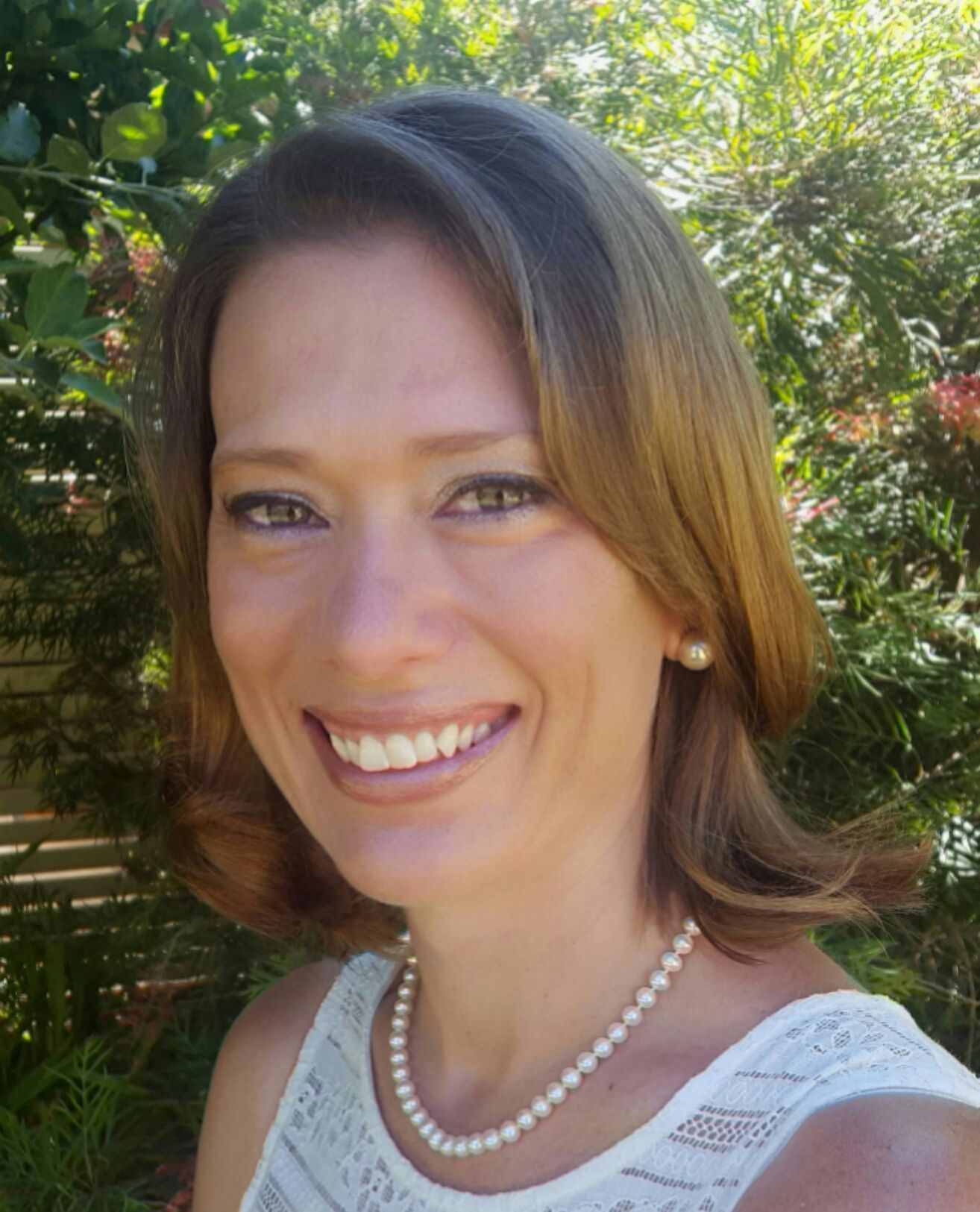 A woman wearing a pearl necklace and earrings is smiling for the camera.