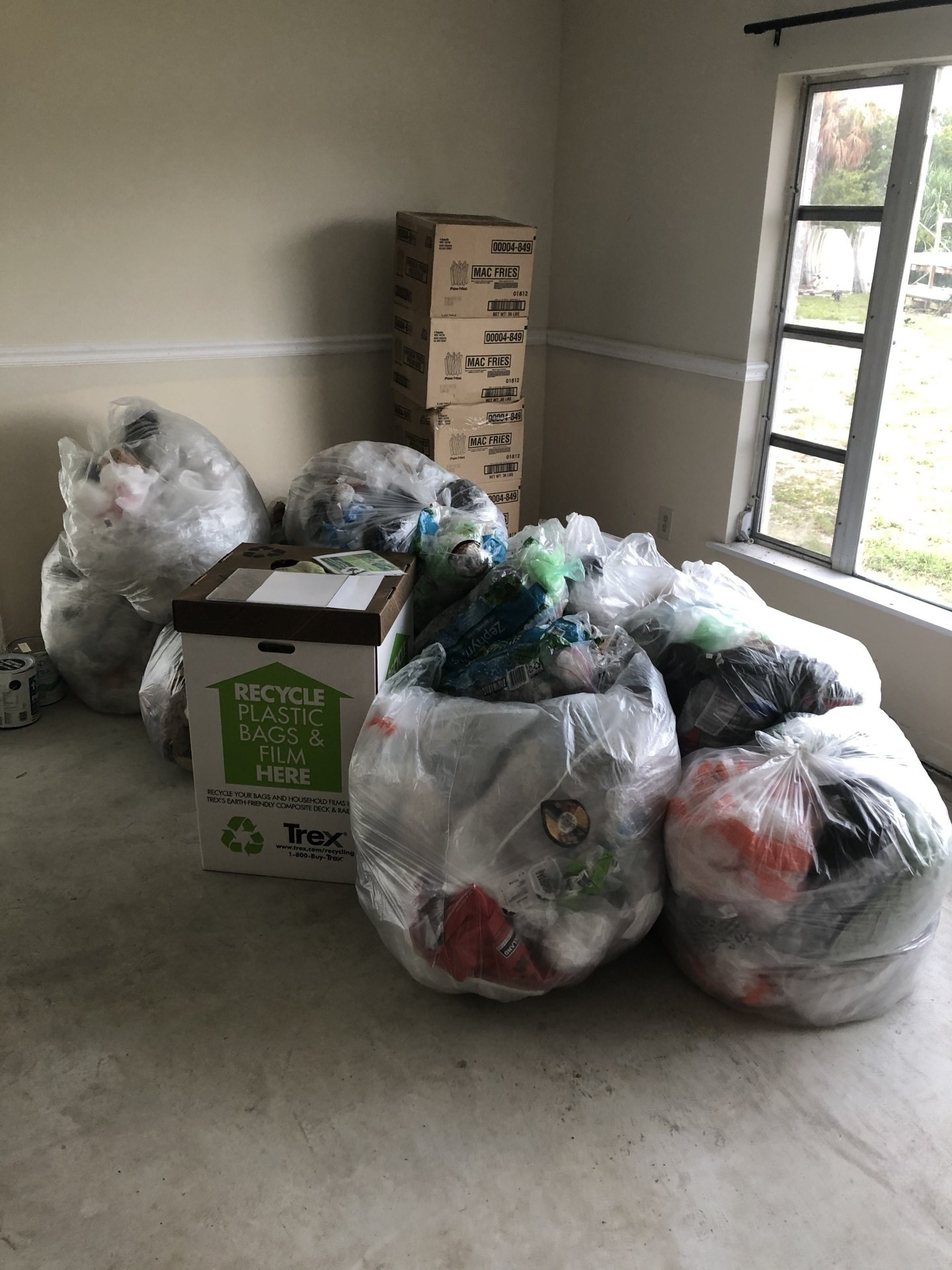 Bags of clothes and cardboard boxes filled with items sit in a room near a window.
