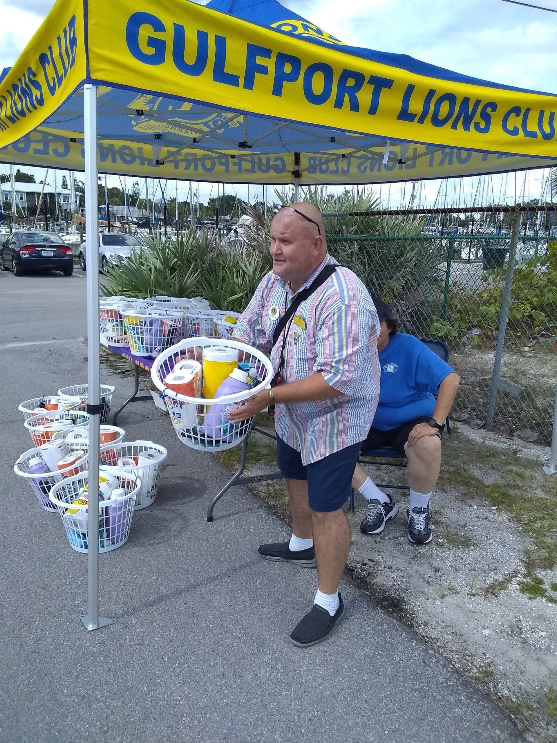 Man holds basket of drinks at Gulfport Lions Club stand. Other volunteers and drinks are in the background.