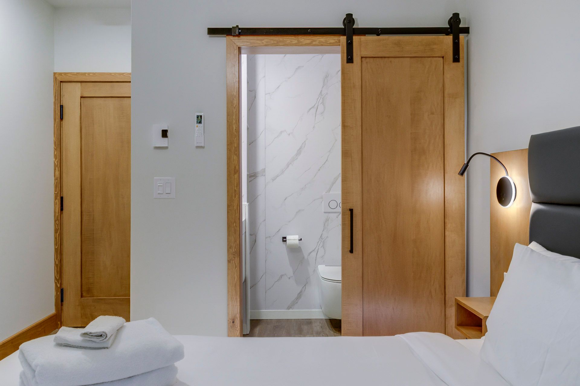 Chambre moderne avec une porte de salle de bain coulissante en bois et un lit soigneusement fait au premier plan