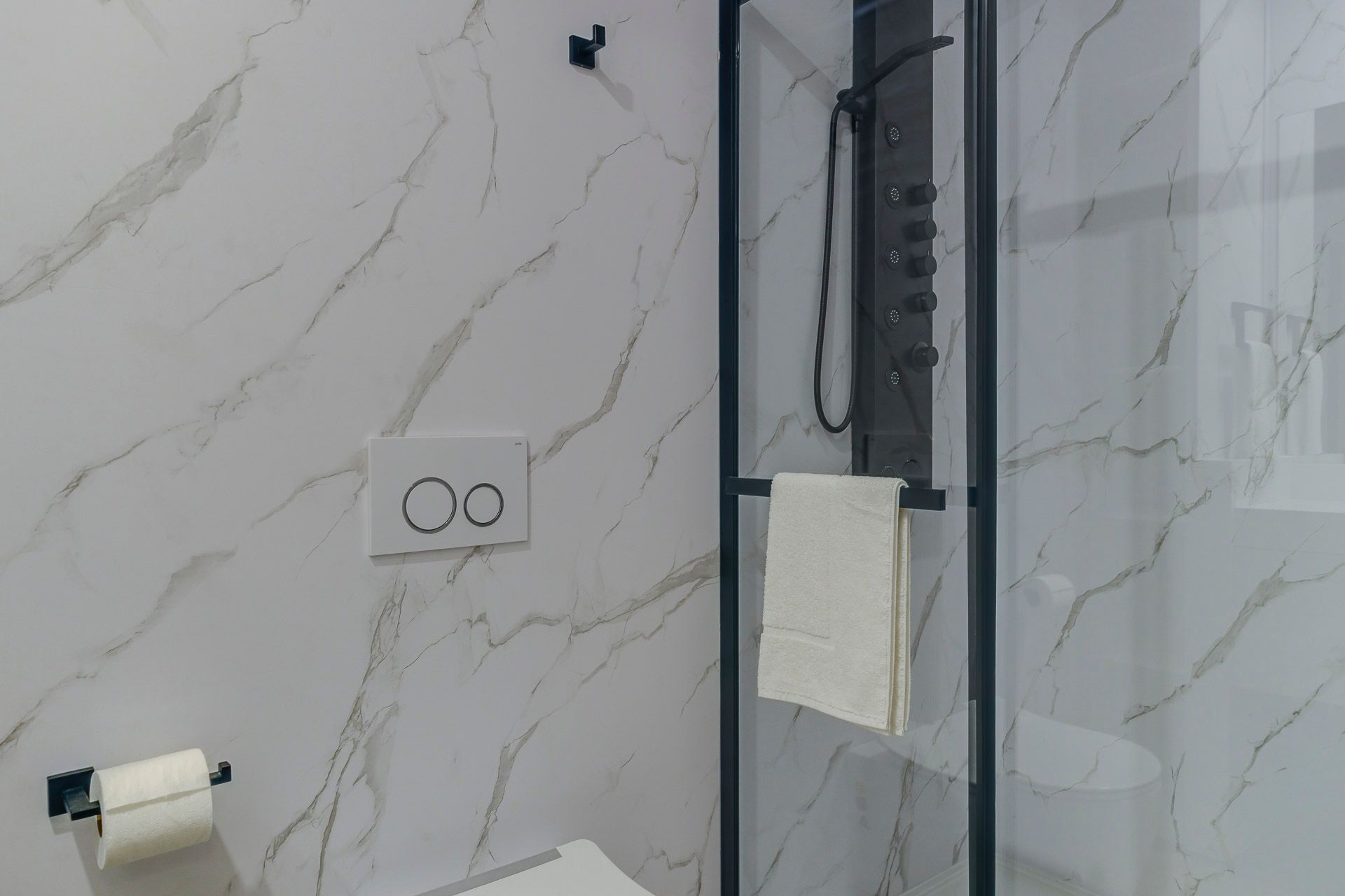 Mur de salle de bain carrelé en marbre avec porte-papier toilette, prise électrique et paroi de douche en verre