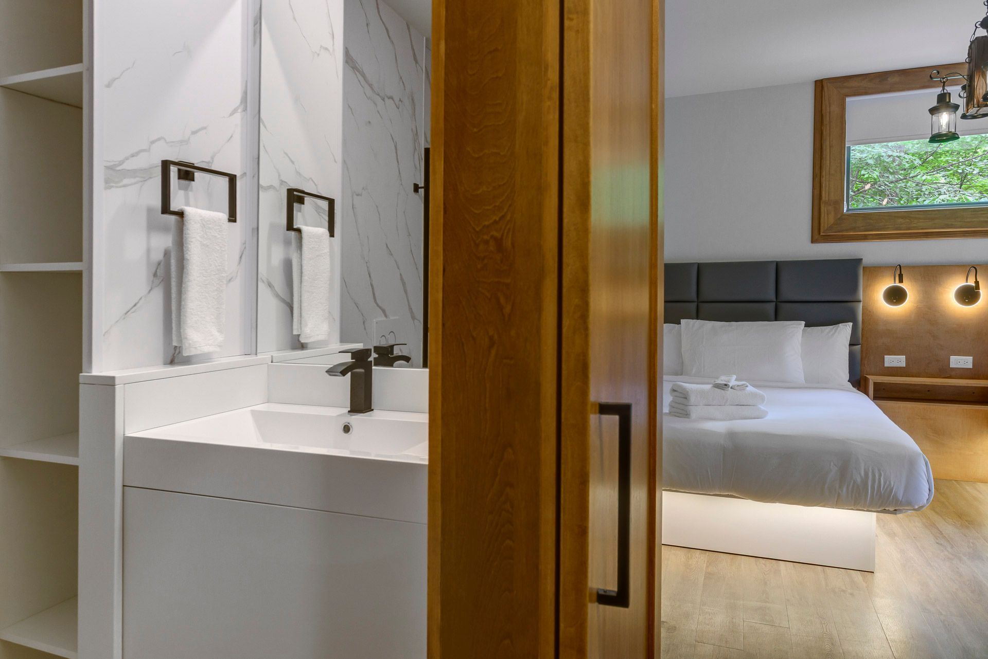 Chambre d'hôtel moderne avec meuble-lavabo et lavabo de salle de bain visibles à travers une porte ouverte