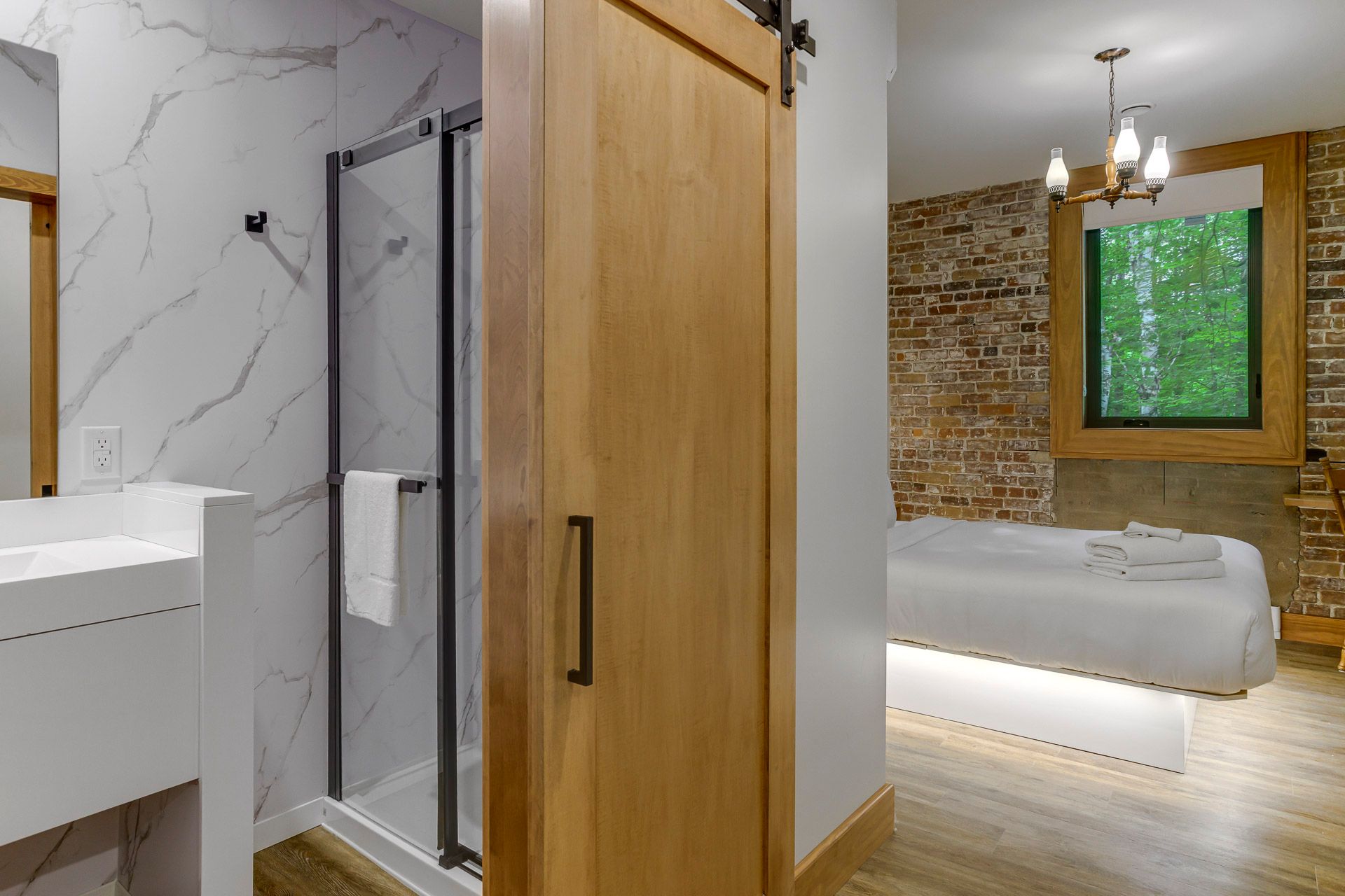 Chambre moderne avec porte coulissante en bois, douche en marbre, mur en briques apparentes et vue sur la verdure.