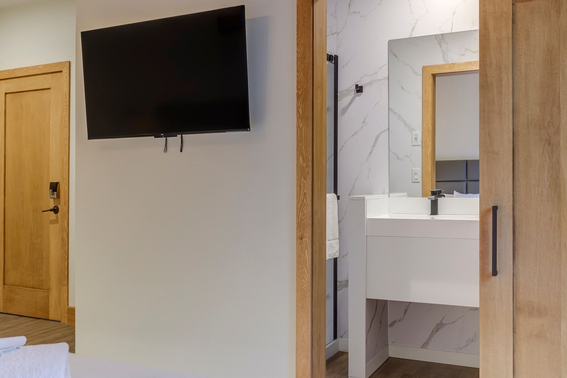 Chambre d'hôtel avec télévision murale et meuble-lavabo de salle de bains visible à travers les portes en bois ouvertes