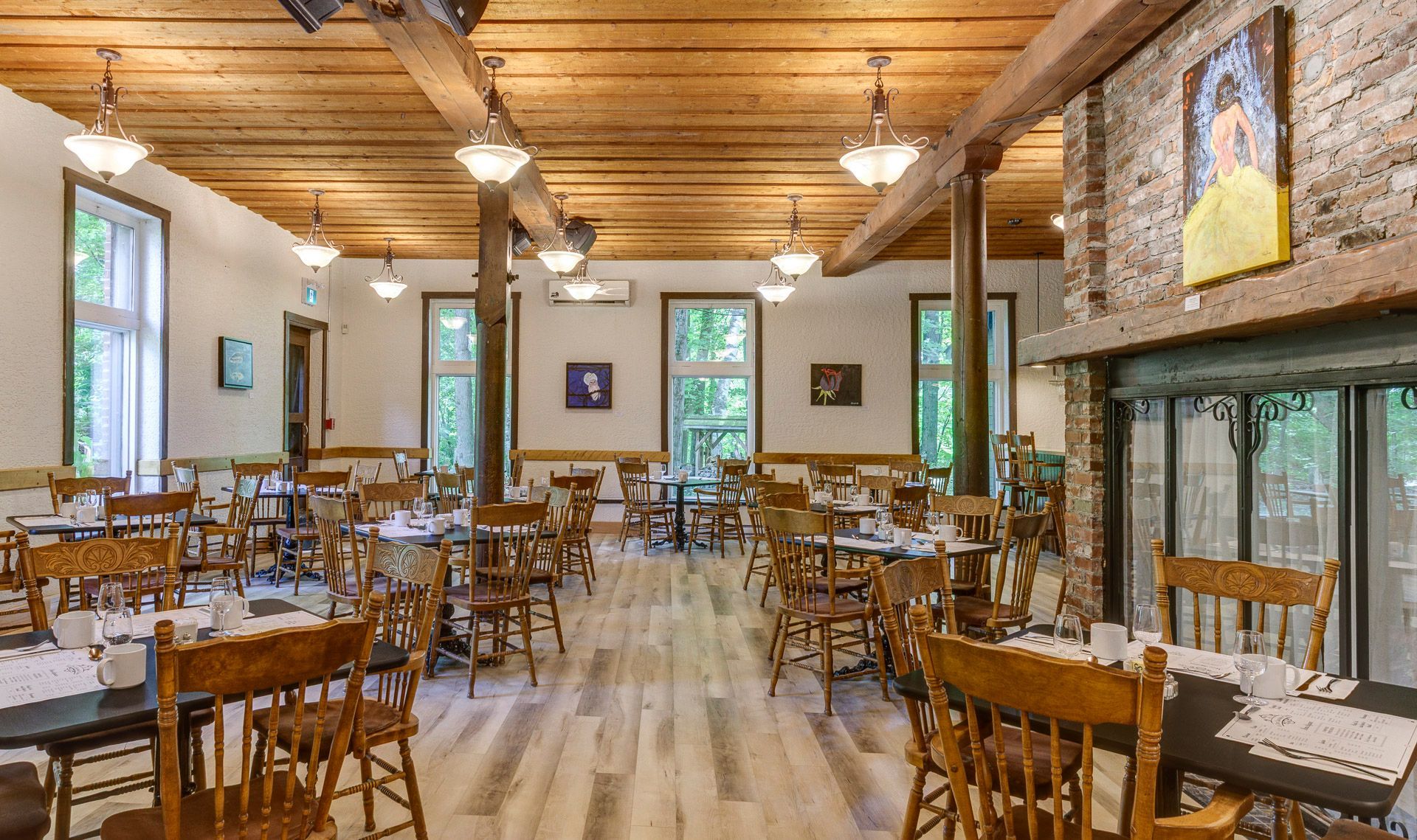 Salle à manger rustique vide avec tables et chaises en bois, poutres apparentes et grandes fenêtres