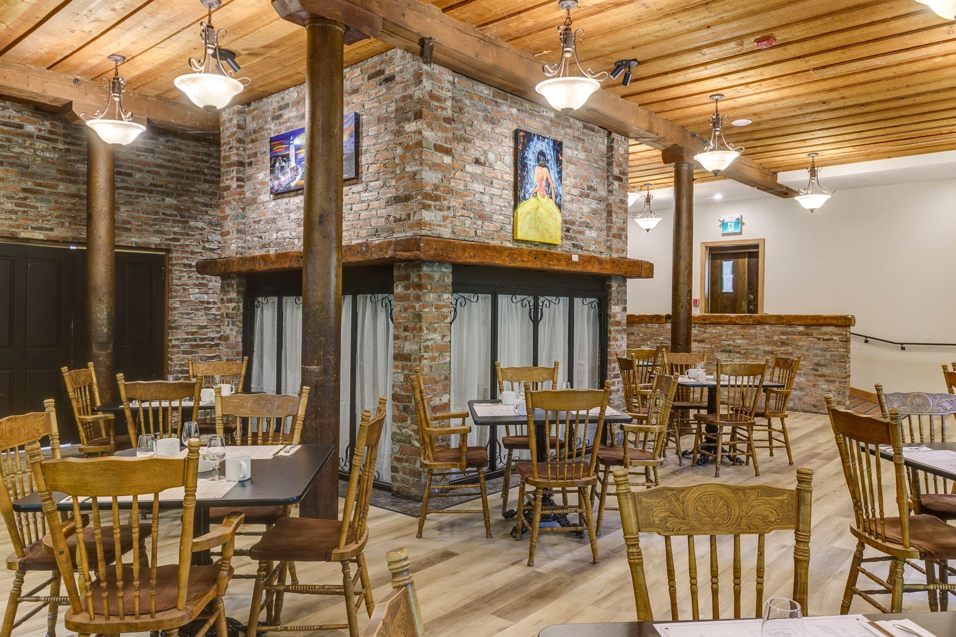 Salle à manger rustique d'un chalet avec cheminée en pierre, plafond en bois et tables et chaises en bois vides