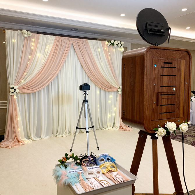 Elegant event photo booth with draped cream and pink backdrop, camera on tripod, and ring light setup