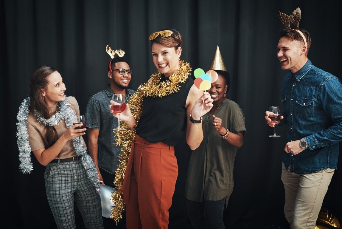 Friends in party hats and leis celebrating, laughing and holding drinks against a dark backdrop