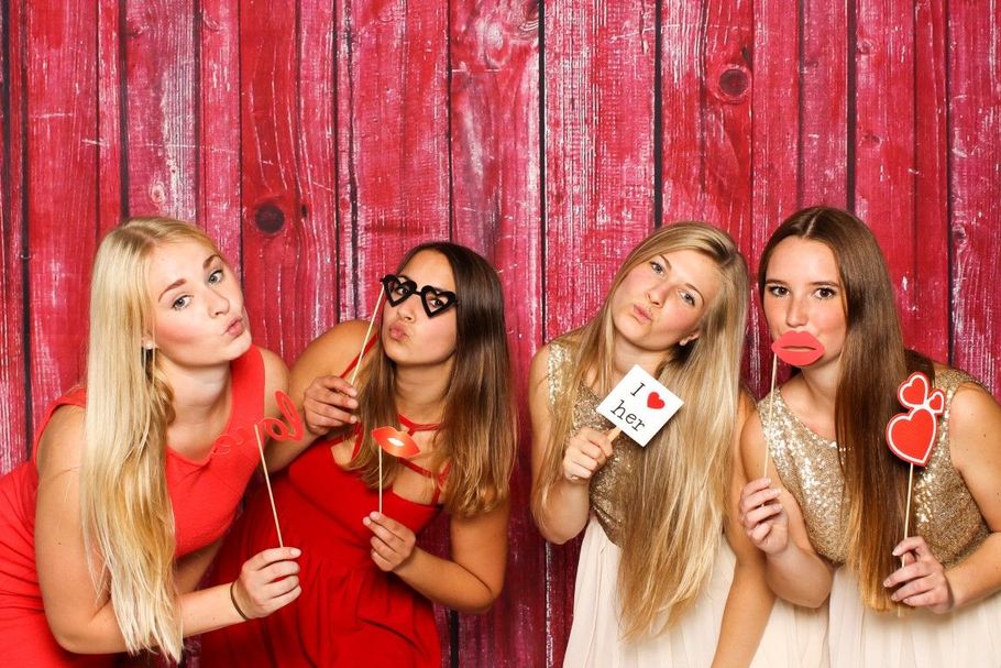 Four women in red and white outfits posing with lollipops against a red wooden wall