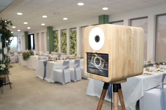 Wooden camera-shaped photo booth on a tripod at a bright banquet hall reception