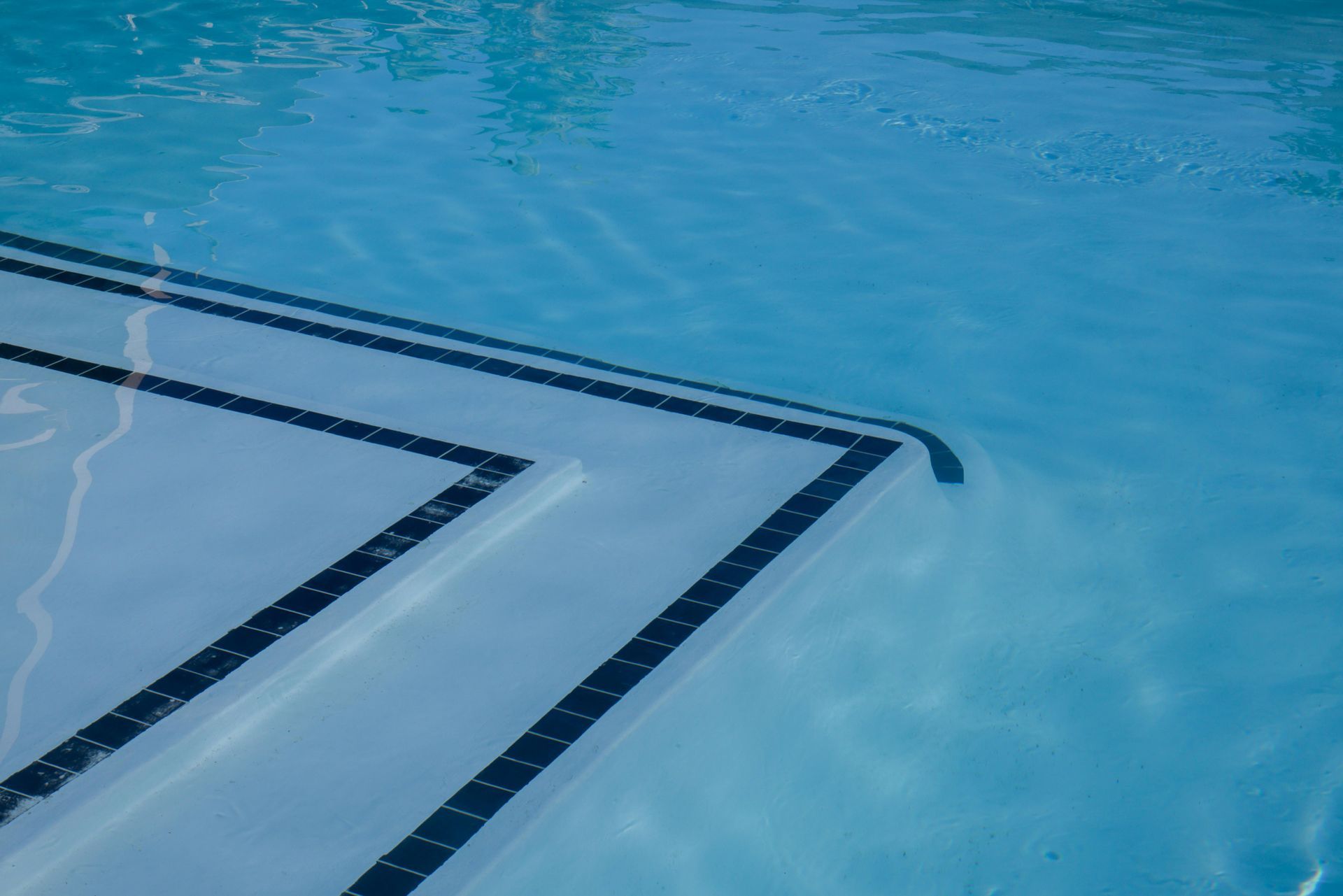 Submerged steps in a swimming pool marked by dark blue tiles against a light blue pool floor.