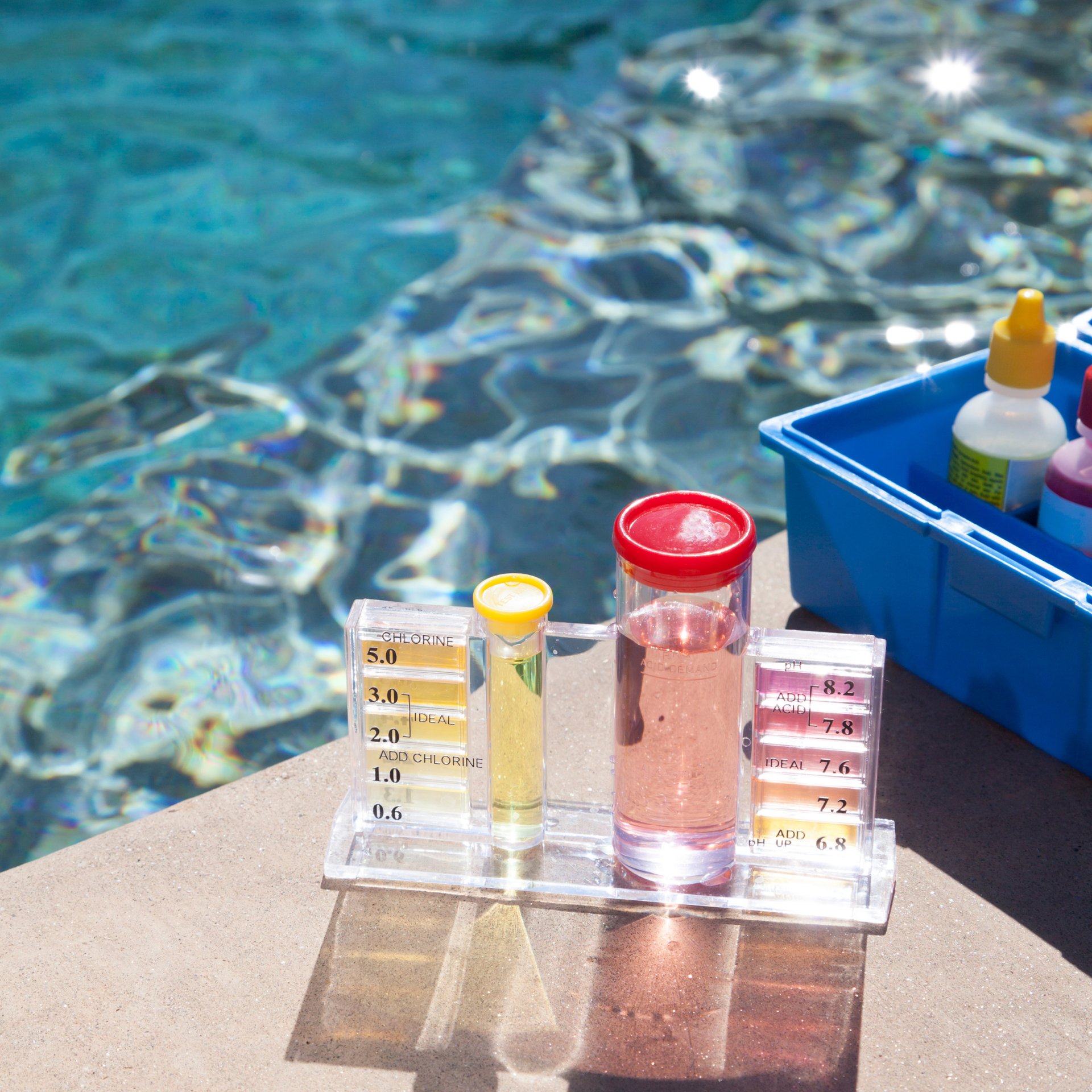Poolside water test kit with sample tubes and a blue supply box on the edge of a pool