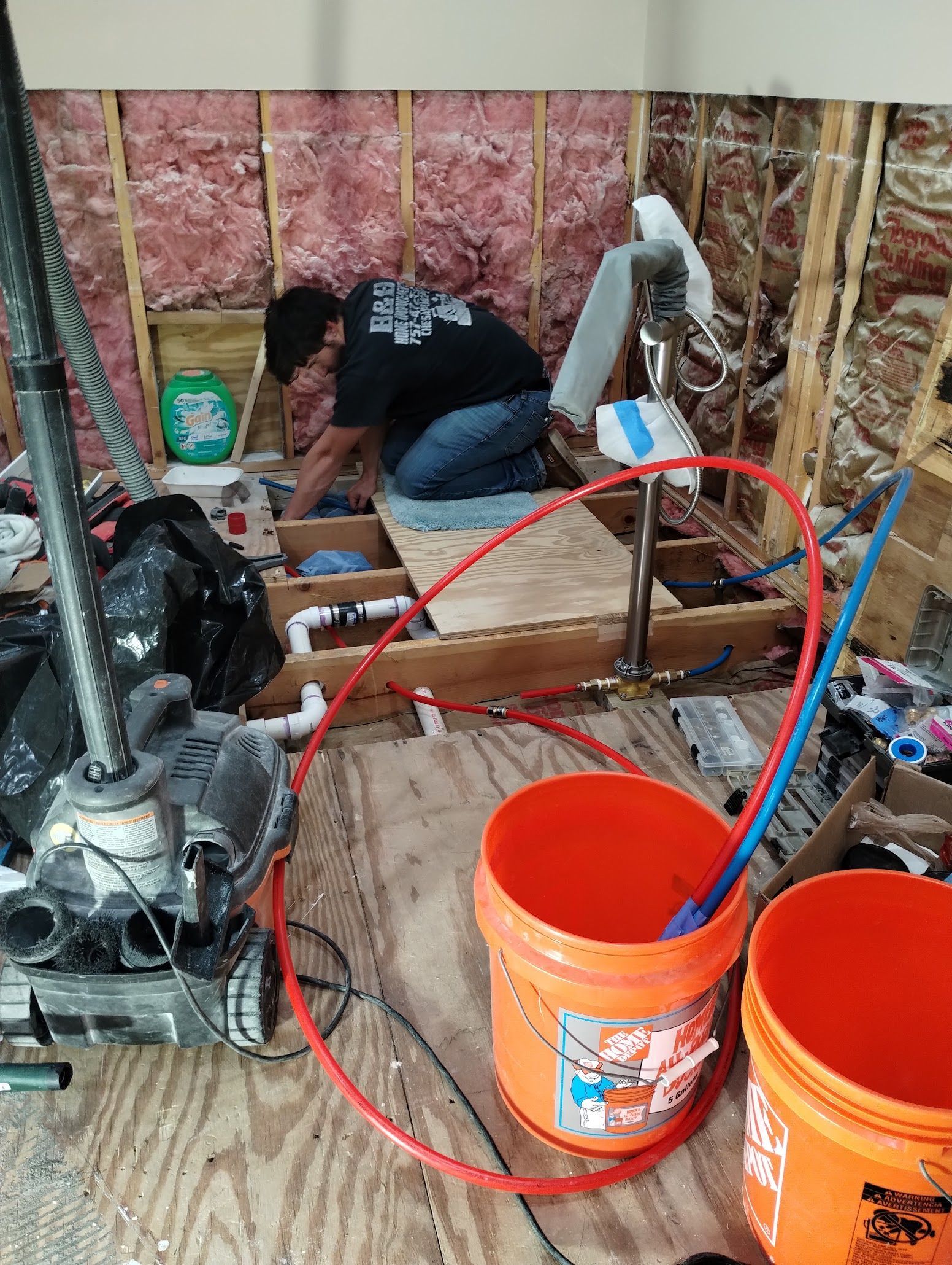 Person working in a construction area with orange buckets and tools, framed by exposed wall studs.