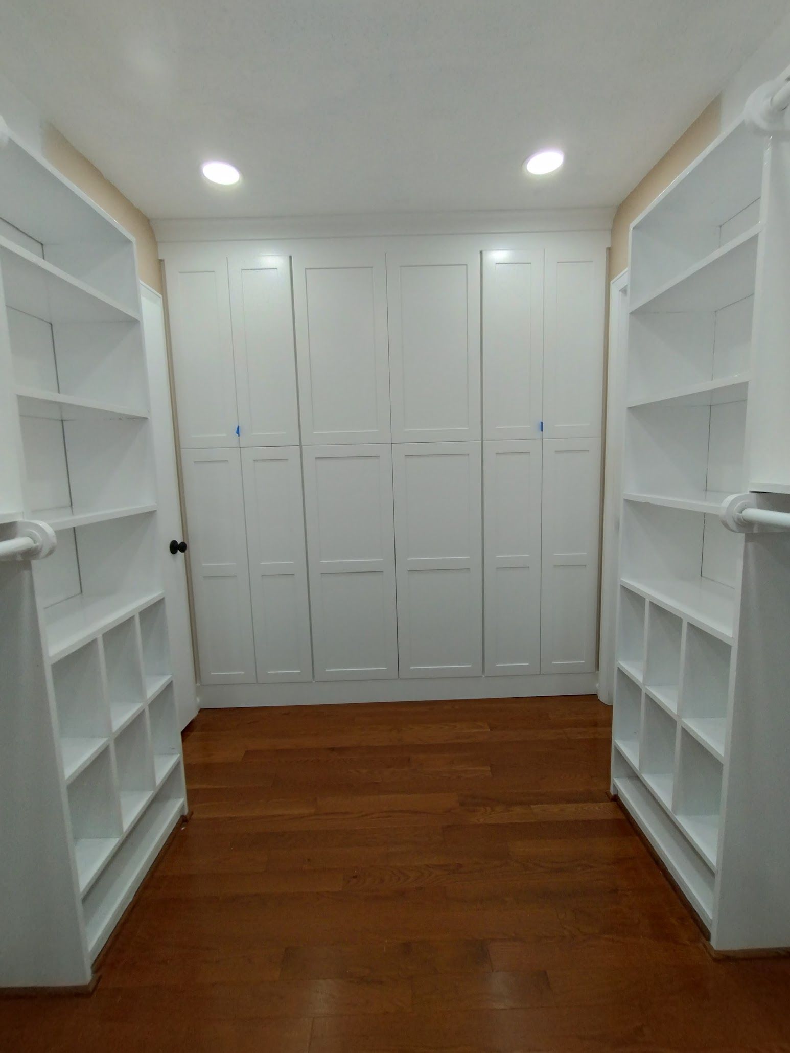 White walk-in closet with built-in shelving, cabinets, and hardwood floor.