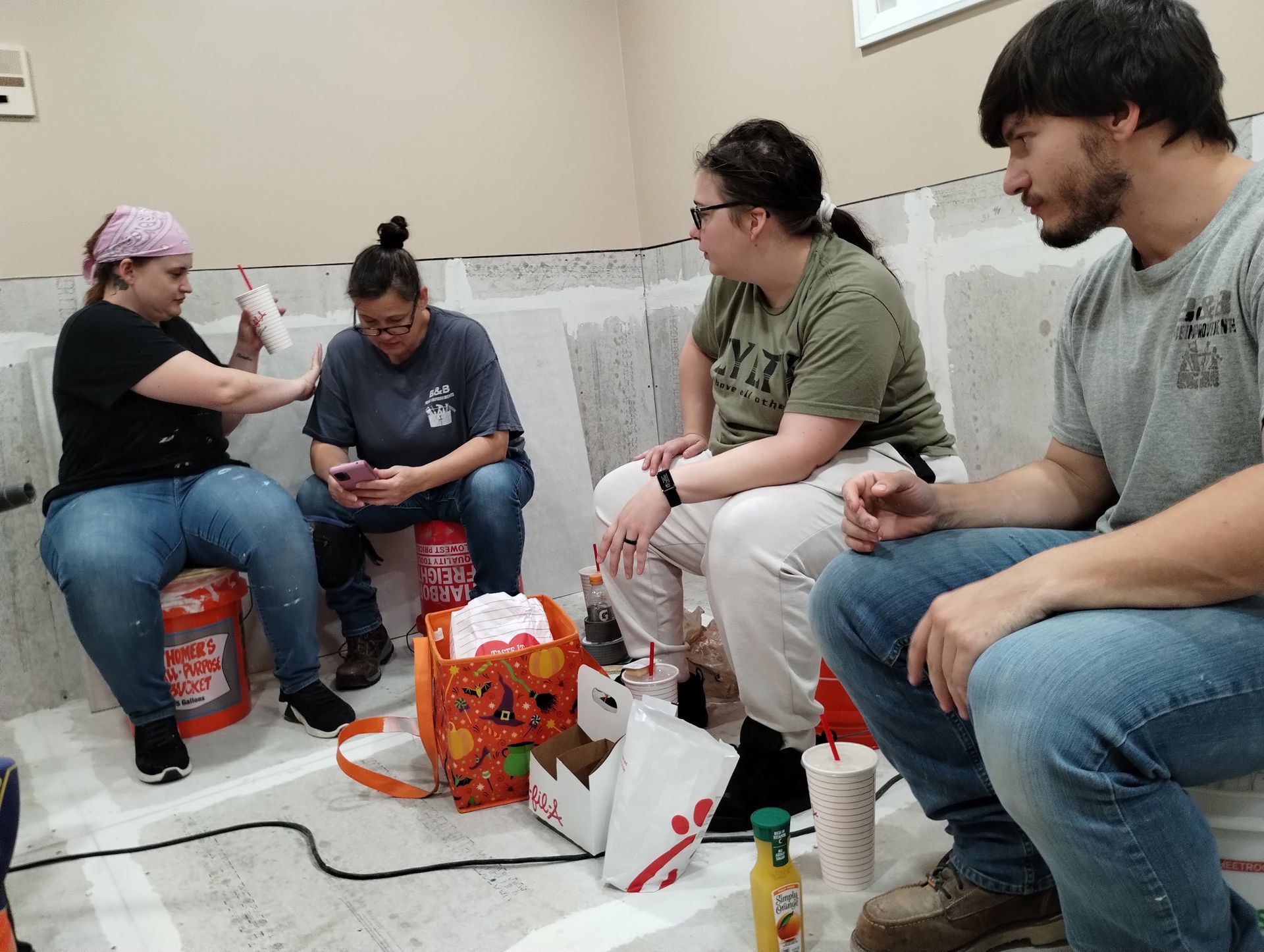 Four people sit on the floor chatting beside a table, surrounded by snacks and gift bags.