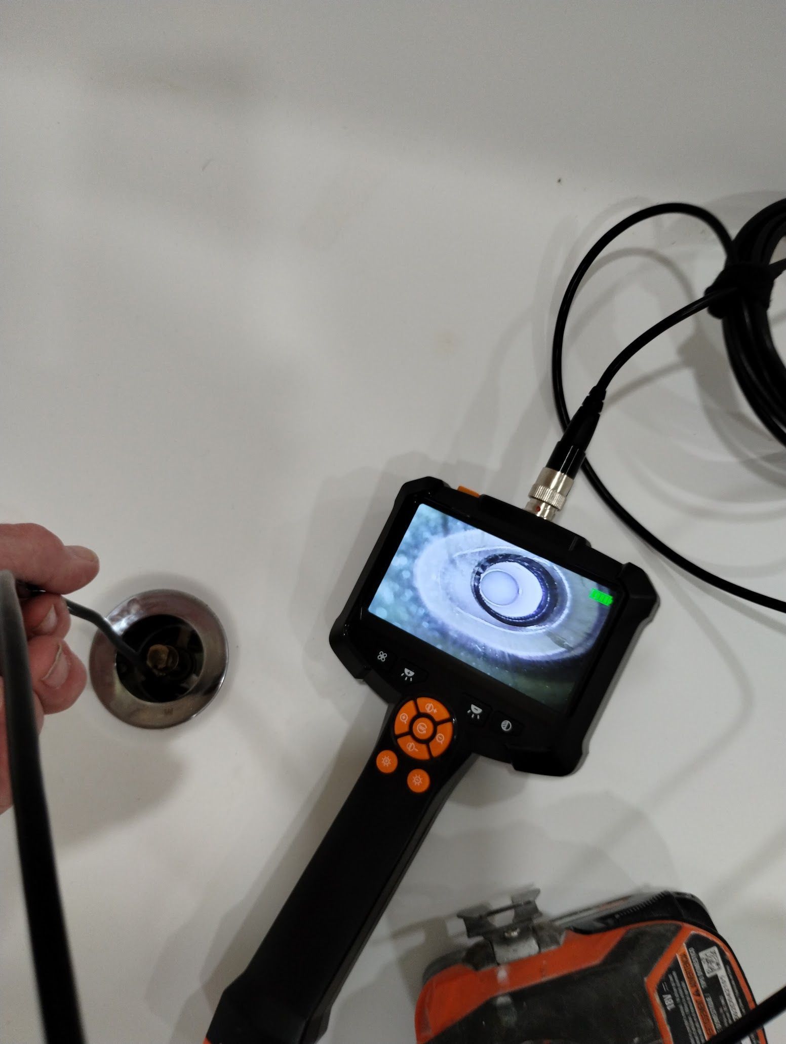 Handheld inspection camera showing a sink drain and plumbing inside a white sink basin