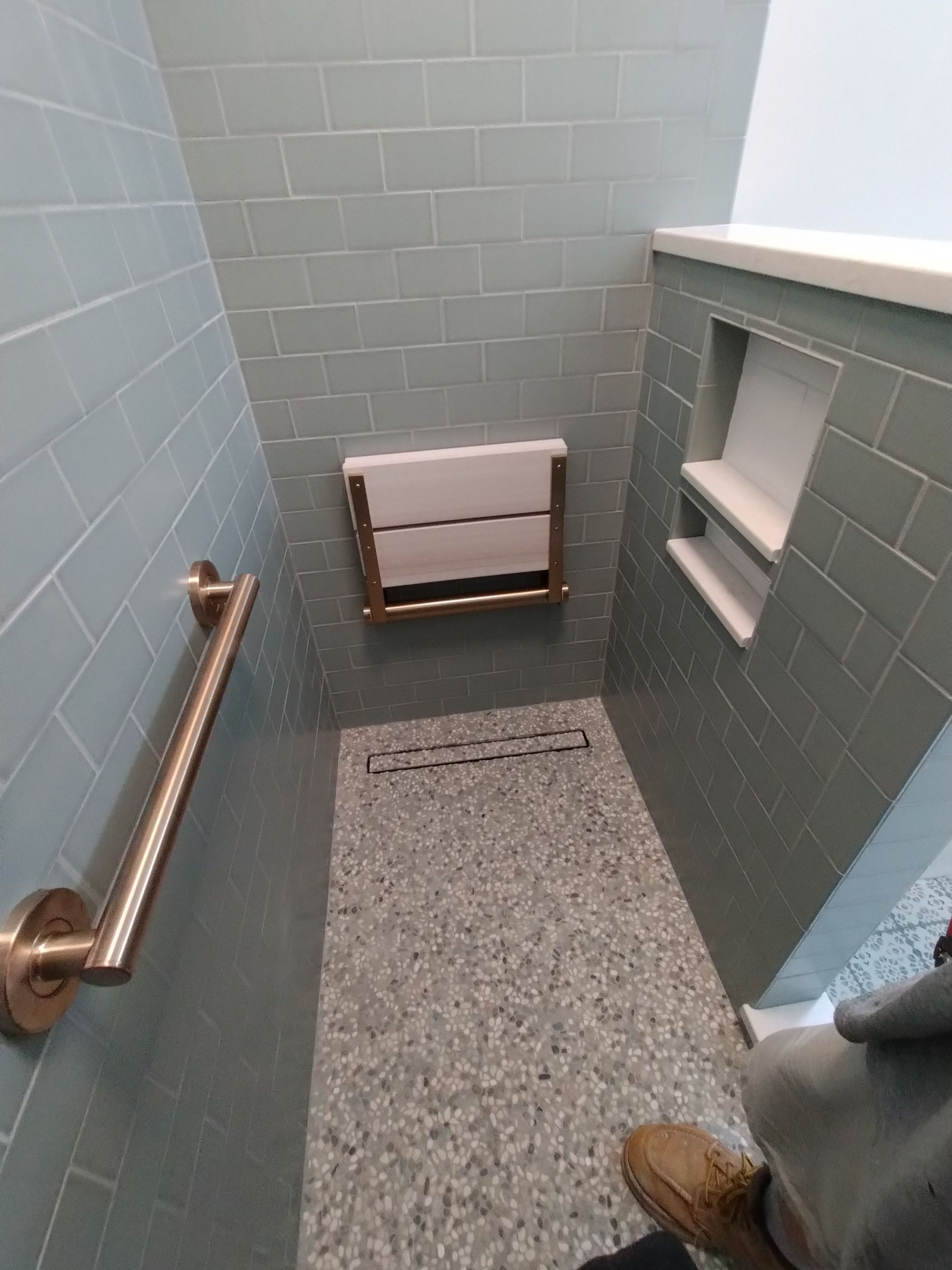 Small tiled restroom with a wall-mounted changing table, grab bars, and a gray-speckled floor.