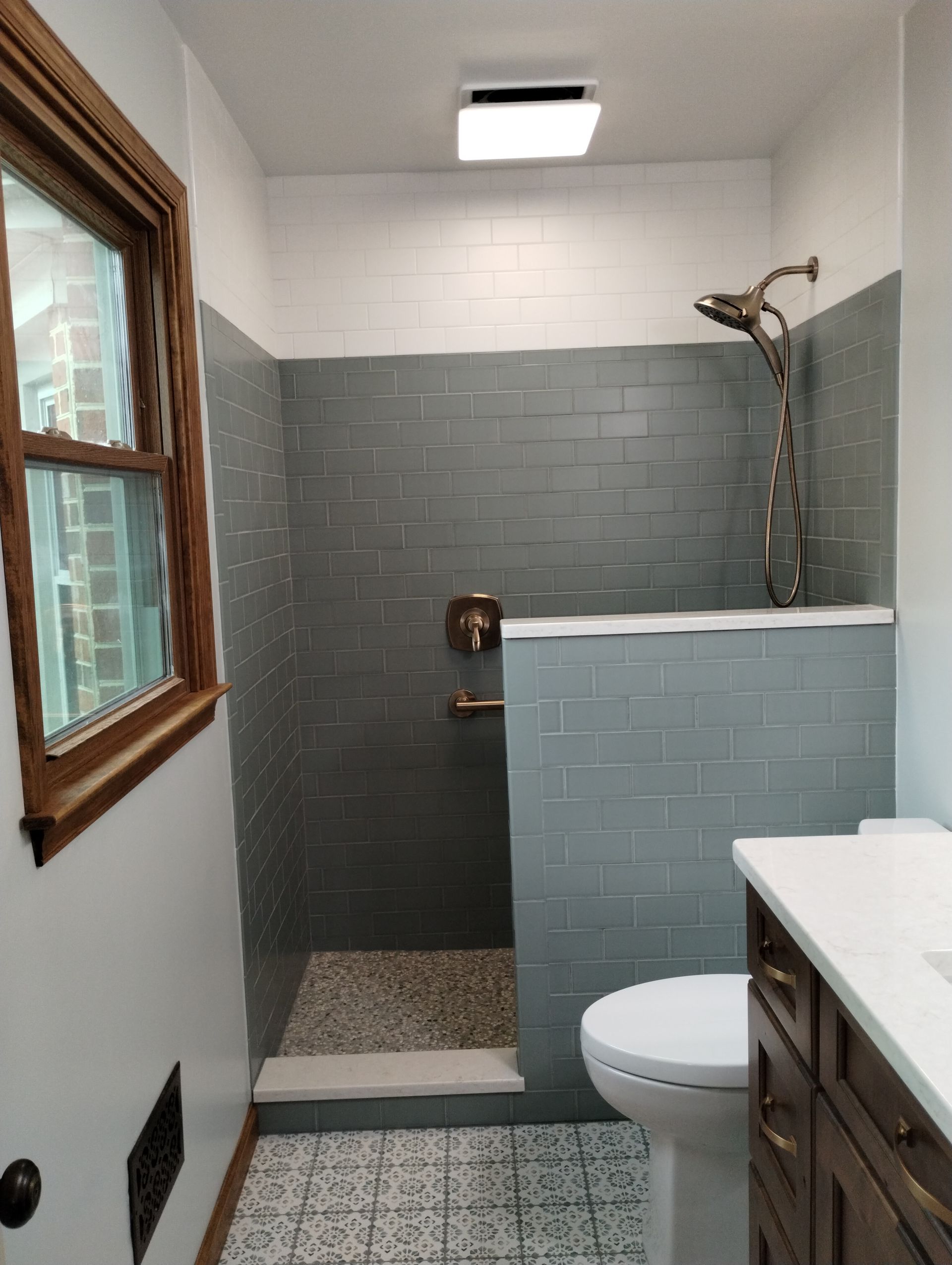 Bathroom with walk-in shower, gray tile, window, toilet, and vanity sink
