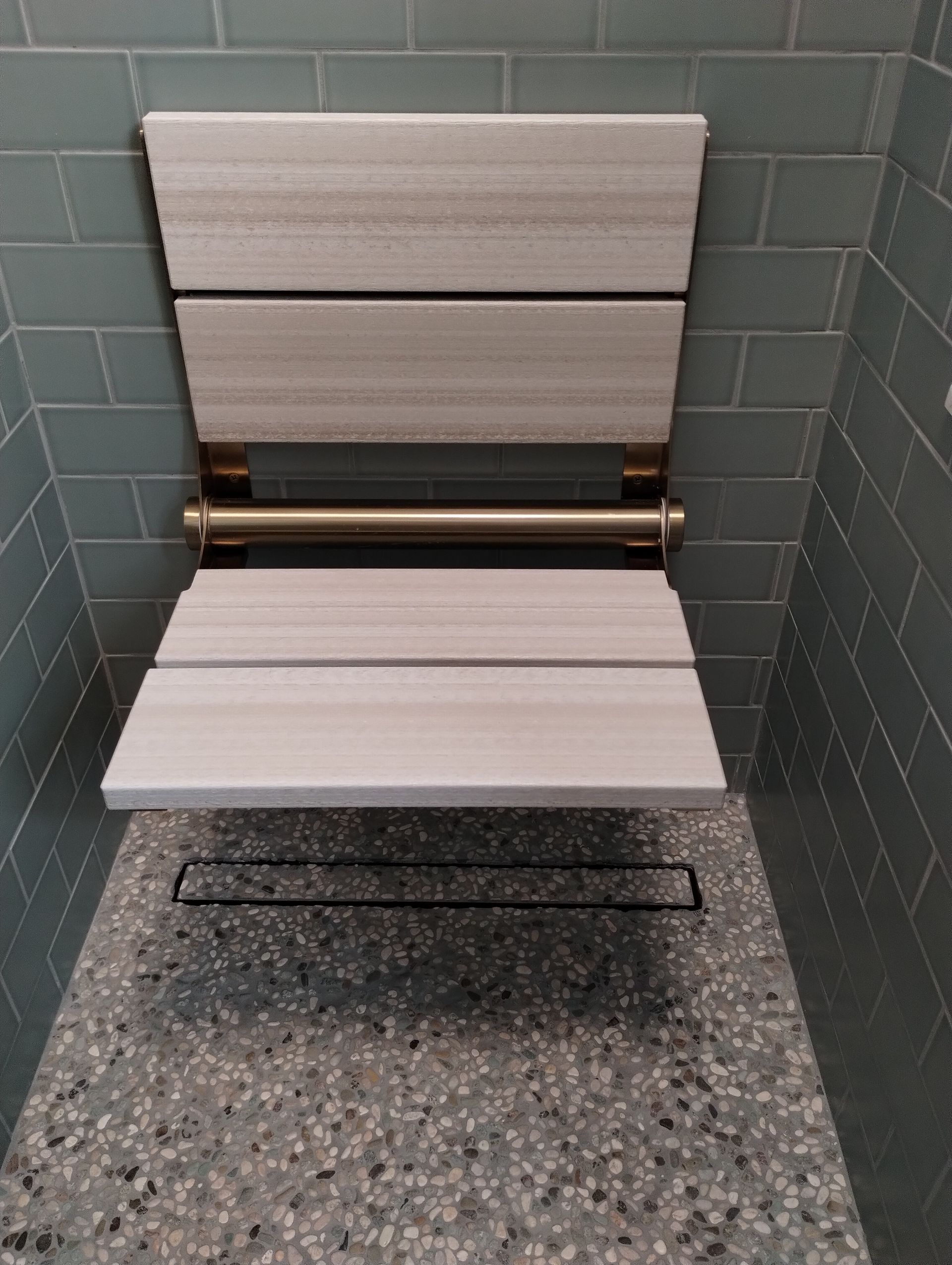 Empty folding shower seat with white slatted panels against gray tiled wall and speckled floor.